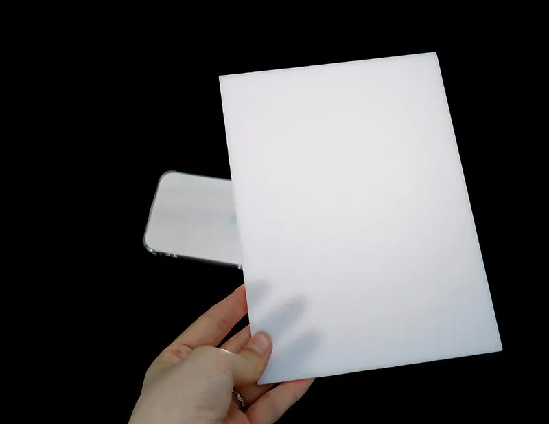 Hand holding a white translucent SinoPlastix PC diffuser sheet in front of a phone screen