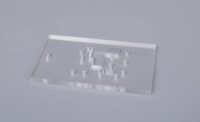 Clear machined plastic sample with holes, raised features and internal cut-outs